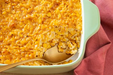 Corn pudding in a casserole dish (with a bit already spooned out from the corner) next to a table napkin