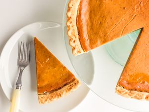 Pumpkin pie on a glass serving platter, and a slice of pie on the plate next to it