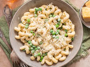 Bowl of Creamy Cavatappi Topped With Shredded Parmesan Next to a Small Bowl With Blocks of Parmesan and Two Forks, All on an Olive Green Kitchen Linen