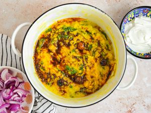 Daal Palak in a Dutch Oven on the Counter Next to a Bowl of Yogurt and a Bowl of Pickled Onions