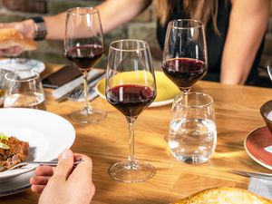 Table settings with people eating dinner and drinking wine. Focus of the photo is the glasses of wine