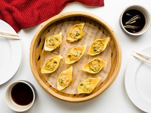 Table Setting: Pork and Chive Dumplings in a Lined Bamboo Steamer, Two Small Bowls of Chinese Vinegar Sauce (One with Sliced Ginger), Two Plates with Chopsticks, and a Kitchen Towel