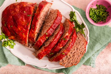 Easy Meatloaf With Some of It Cut Into Slices on a Platter and Sitting on a Sage Table Napkin Next to a Small Bowl With Sliced Parsley