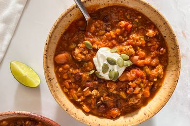 Bowl of easy pumpkin chili topped with a dollop of sour cream and pumpkin seeds at a table setting with another bowl of chili, a lime wedge on the counter, and white table napkins