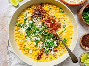 Bowl of Esquites Topped with Cilantro, Cotija Cheese, and Ancho Chile Pepper Surrounded by Bowls of Toppings