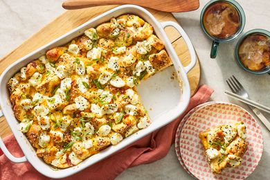 Everything bagel sandwich casserole in a casserole dish at a table setting with a serving on a plate, utensils, and cups of coffee