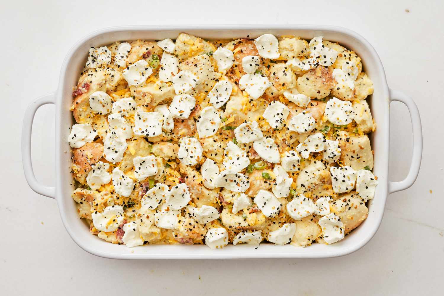 everything bagel sandwich bagel mixture added to the casserole dish and topped with cream cheese dollops and everything bagel seasoning