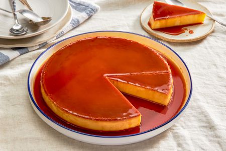 Plate of flan at a table setting with a serving on a plate and a stack of plates with utensils 