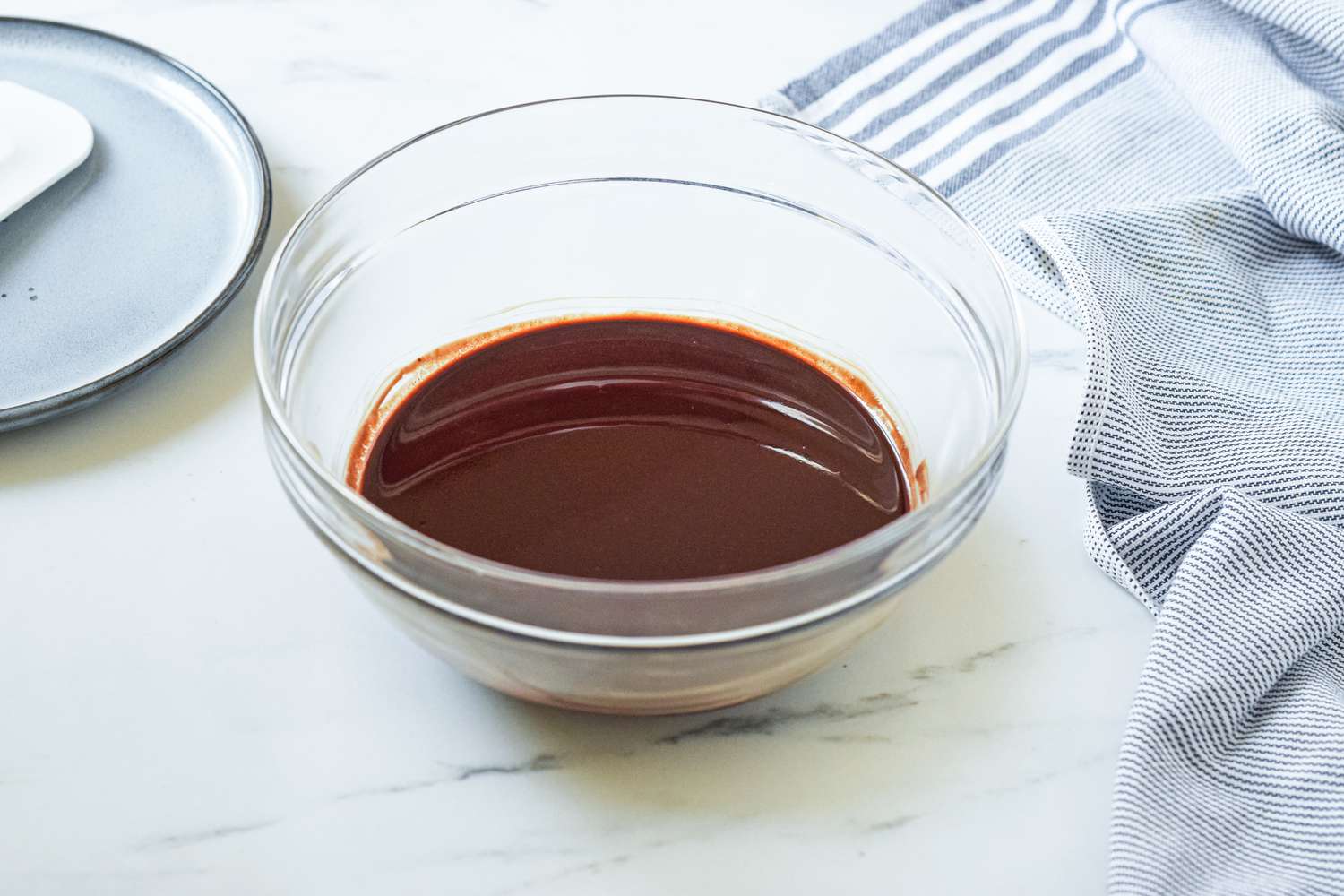 Bowl of melted chocolate and butter, , and next to the bowl, a spatula resting on a small plate and a blue and white kitchen towel for fluffernutter brownie recipe