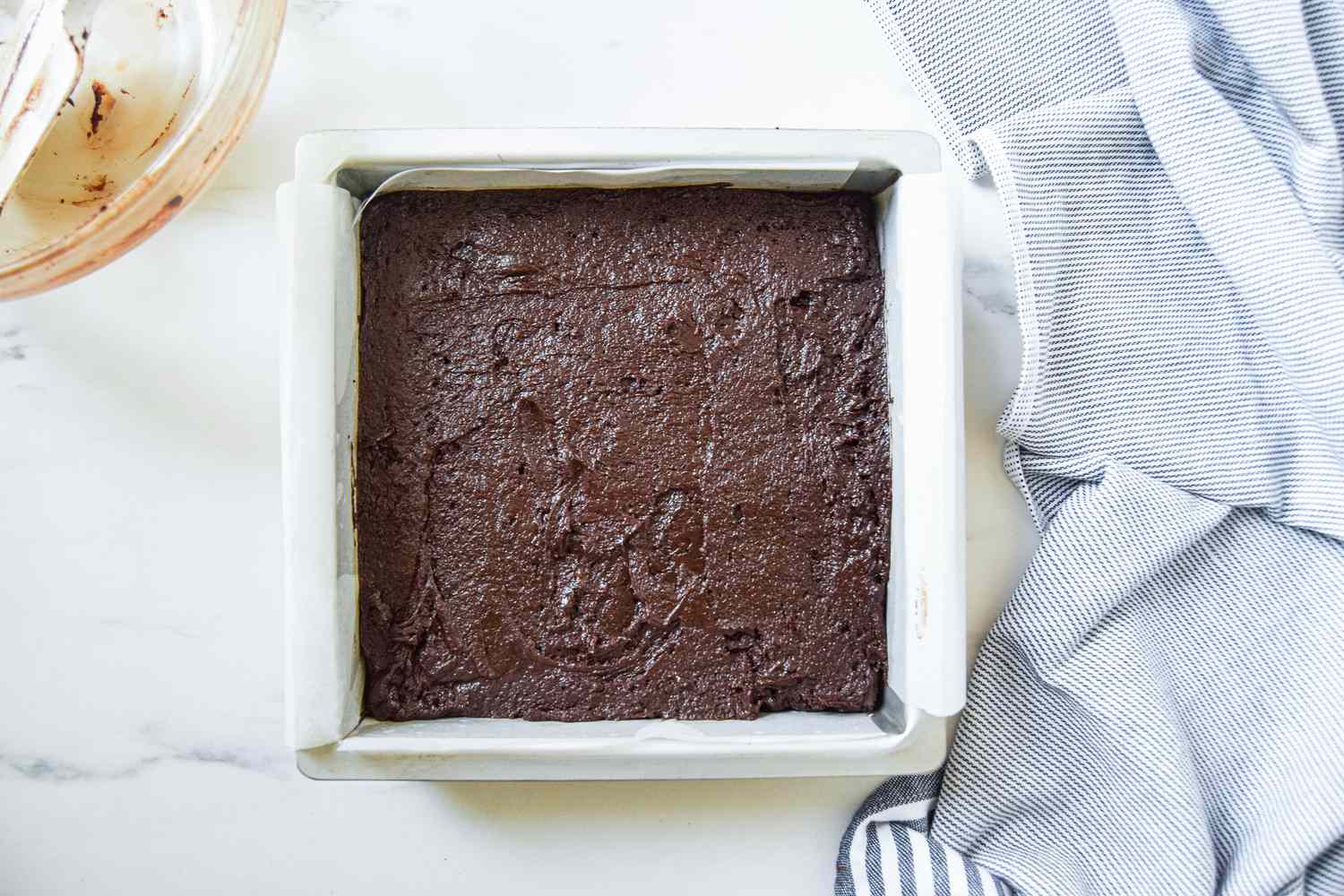 Fluffernutter brownie butter spread evenly into the baking pan, and next to it, the blue and white striped kitchen towel