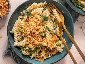 Bowl of Fusilli With Spring Vegetables and Breadcrumbs Next to a Glass, a Bowl of Breadcrumbs, and a Another Bowl of Pasta