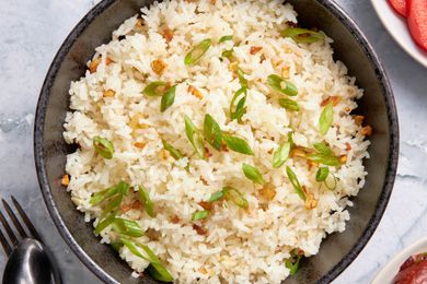 Bowl of Garlic Fried Rice (Sinangag na Kanin) next to some utensils and plates with sides