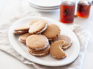 Platter of gingerbread cookies filled with lemon frosting with two cups of tea behind the platter.