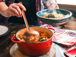 Someone serving soup with a ladle from a Dutch oven to a blue bowl