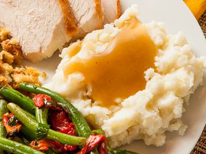 Plate of thanksgiving dinner: slices of turkey, stuffing, green beans and roasted bell peppers, and a mashed potatoes with gravy