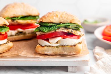 Grilled Chicken Caprese Sandwiches on a Parchment Lined Tray, and on the Counter Next to the Tray, Plates With Individual Ingredients 