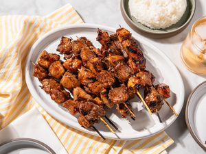 Grilled pork skewers on a white platter with rice on the side