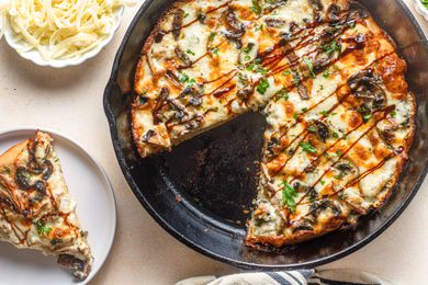 Gruyère Mushroom Pizza with Balsamic Glaze in a Cast Iron Skillet Next to a Plate with a Slice of Pizza and a Bowl of Shredded Cheese