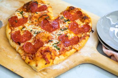 Heart-Shaped Pepperoni Pizza on a Pizza Peel Next a Stack of Plate 