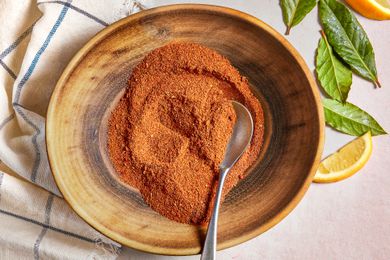 Bowl of Old Bay Seasoning With a a Spoon, Sitting on a White Kitchen Towel Next to Lemon Leaves and Lemon Wedges