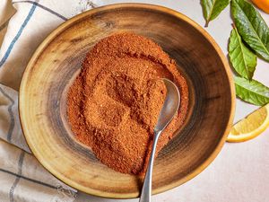 Bowl of Old Bay Seasoning With a a Spoon, Sitting on a White Kitchen Towel Next to Lemon Leaves and Lemon Wedges