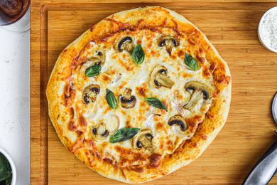 Overhead view of a pizza dough recipe and topped with cheese and mushrooms.