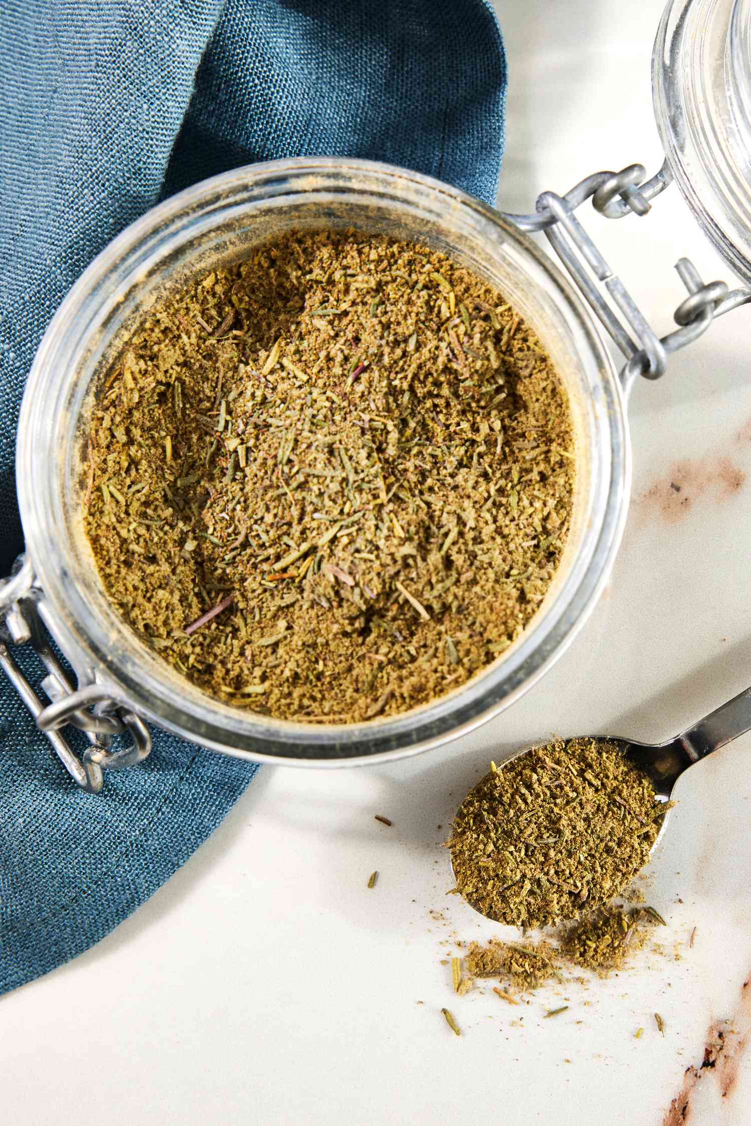 Jar of Poultry Seasoning With a Spoonful of Seasoning Next to a Navy Blue Table Napkin 