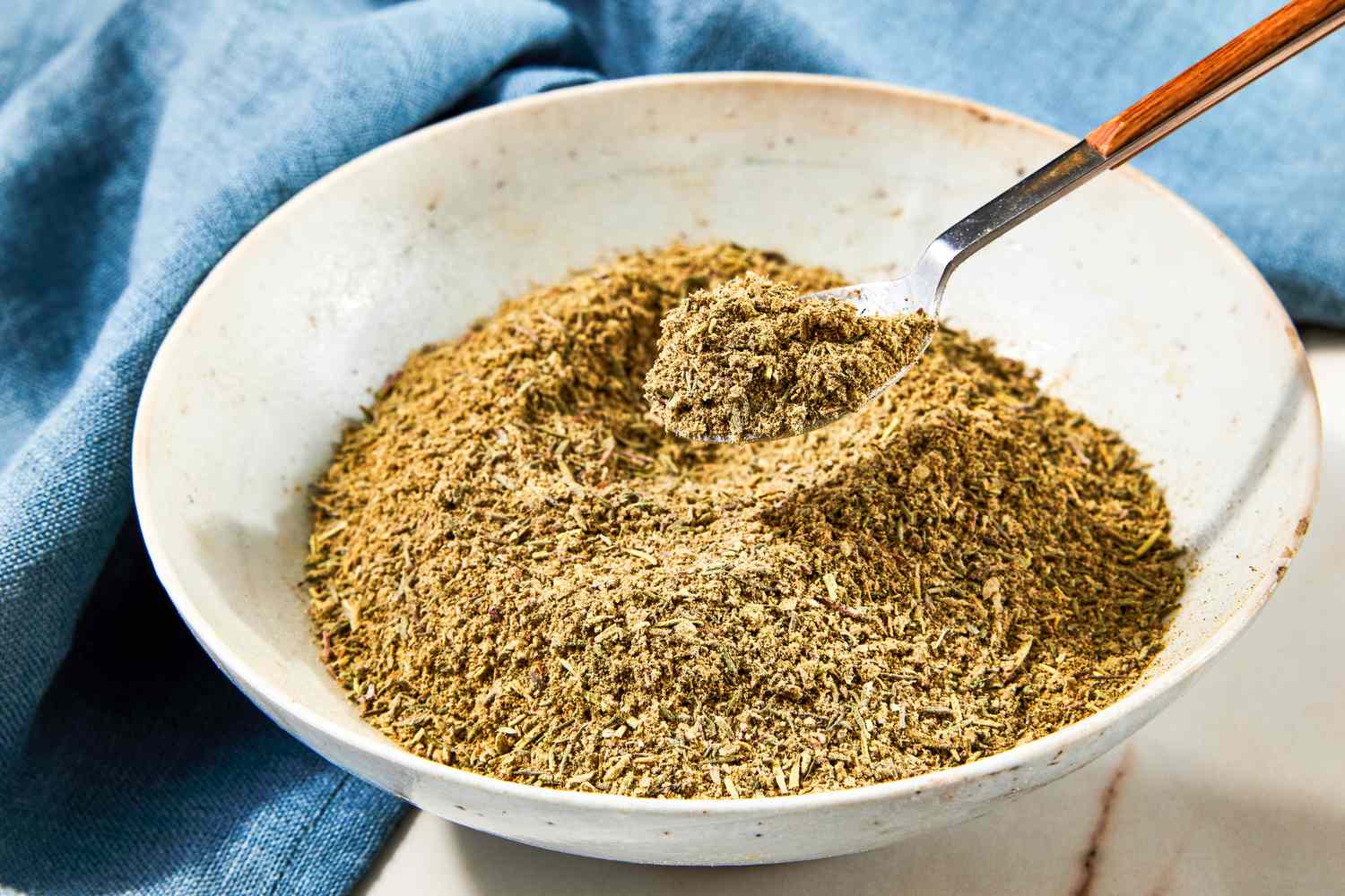 Bowl of of Poultry Seasoning With Spoon in the Bowl, Next to a Navy Blue Table Napkin 