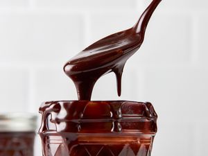 Hot fudge sauce cascading into a pint jar from a spoon 
