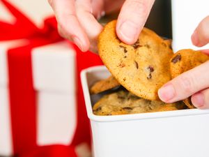 hand packing a white tin box with chocolate chip cookies