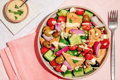 Bowl of salad topped with hummus salad dressing, and in the surroundings, a bowl of hummus salad dressing on a white coaster and a pink table napkin