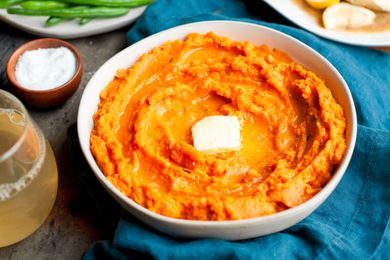 Table Setting with a Bowl of Instant Pot Mashed Sweet Potatoes Topped with Butter, a Plate of Green Beans, a Platter of Chicken, a Small Bowl of Salt, a Drink, and a Table Napkin