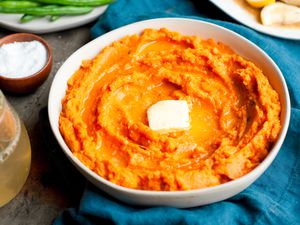 Table Setting with a Bowl of Instant Pot Mashed Sweet Potatoes Topped with Butter, a Plate of Green Beans, a Platter of Chicken, a Small Bowl of Salt, a Drink, and a Table Napkin