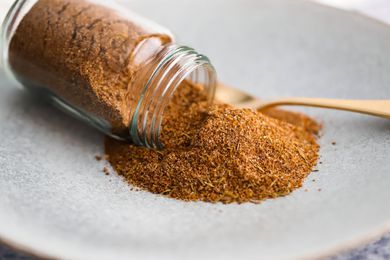 Jerk Seasoning Cascading From a Small Jar Onto a Plate With a Spoon for Jerk Spice Seasoning Recipe