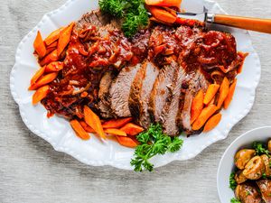 Jewish Brisket on a Plate with Carrots and Parsley and a Bowl of Potatoes