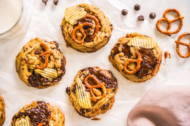 Kitchen Sink Cookies, Pretzels, Chocolate Chips, and a Glass of Milk on a Piece of Crumpled Parchment Paper and a Mauve Kitchen Linen