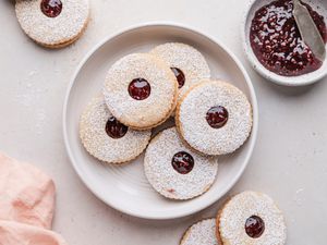 Jam filled sandwich cookies on a plate with additional cookies and jam set around the plate.