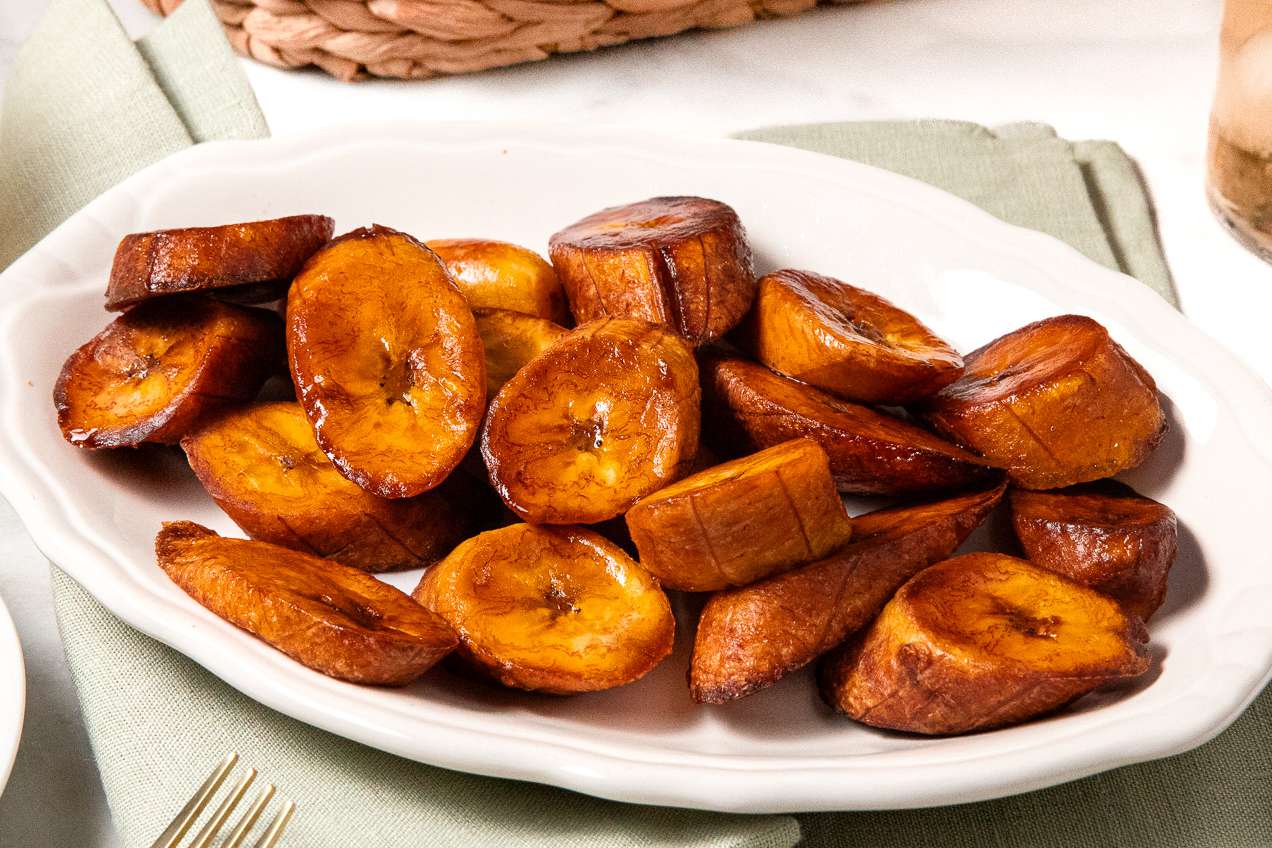 Maduros (Fried Sweet Plantains) on a Plate, and in the Surroundings, a Light Olive Green Kitchen Towel and a Woven Basket