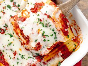 Manicotti Removed From Casserole Dish Filled With Manicotti Using a Wooden Spoon