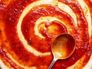 Tomato sauce on a raw pizza dough with a large spoon
