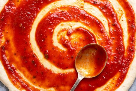 Tomato sauce on a raw pizza dough with a large spoon