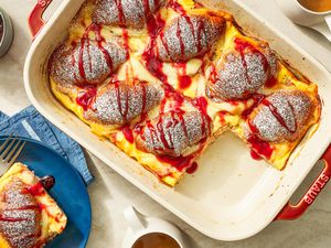 Monte Cristo croissant casserole in a casserole dish and in the surroundings, a serving on a small plate with a fork, a container of jelly, and cups of coffee