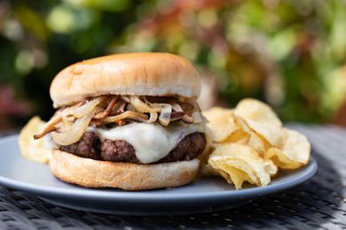 Side view of a mushroom and swiss burger on a plate with chips outside.