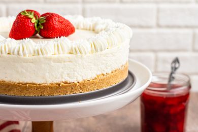 Side view of a A cake stand with no bake cheesecake topped with fresh strawberries.