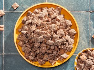 Bowl of nutella puppy chow next to a smaller bowl with more on a counter with some pieces of puppy chow scattered around