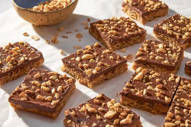 Oh Henry bars on a crinkled parchment paper with a bowl of crushed peanuts 