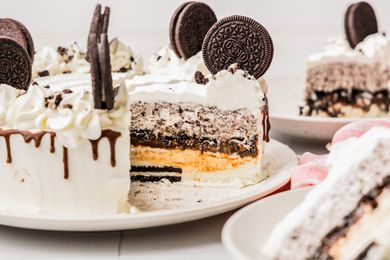 Oreo Ice Cream Cake on a Plate With Some of the Cake Cut Into Slices, and in the Surroundings, Slices on Two Plates and a Kitchen Towel on the Counter