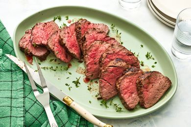 Sliced Oven Roasted Fillet of Beef on a Plate, and in the Surroundings, the Carving Utensils on the Green Kitchen Towel, Two Glasses of Water, and a Stack of Plates