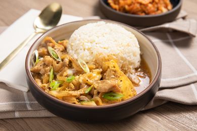 Microwave Oyakodon and Rice in a Small Plate Surrounded by a Table Setting with a Spoon, a Table Napkin, and a Small Plate with Kimchi