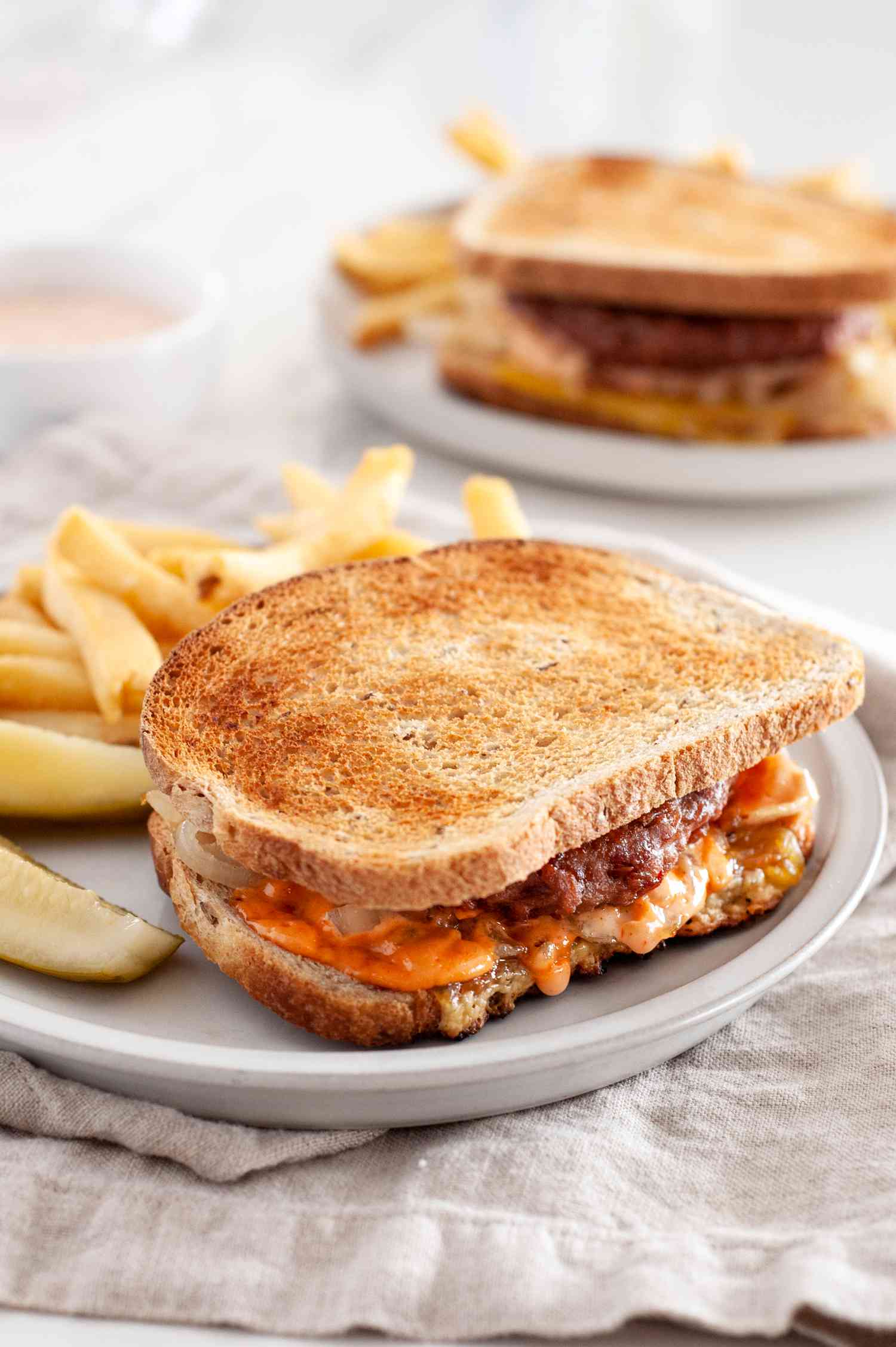 Vegan Patty Melt with Fries on a Plate over a Table Napkin, and in the Background, Another Plate with More